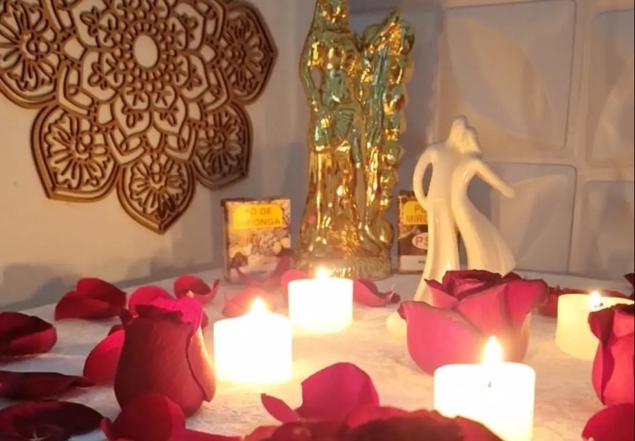 Altar com a mandala dourada entalhada na parede, imagem dourada, velas brancas acesas e pétalas de rosa