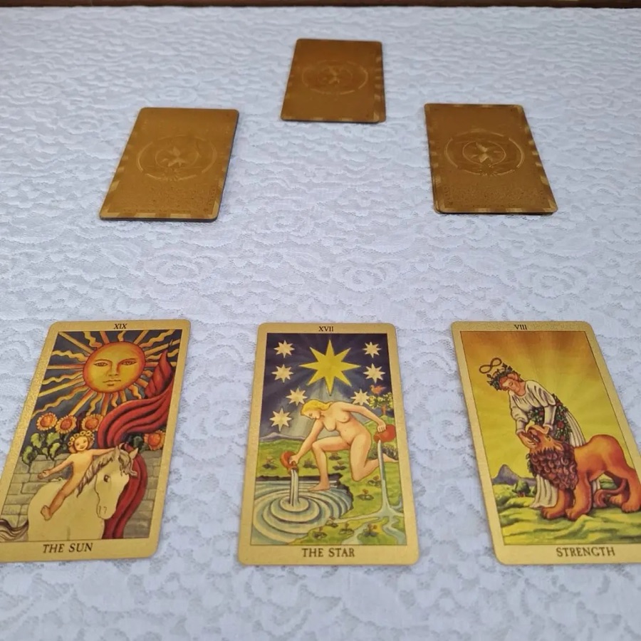 Tiragem de tarot sobre a toalha branca: O Sol, A Estrela e A Força abertas, com três cartas douradas acima